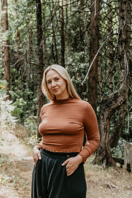 Woman in a brown top and black pants standing in a forest