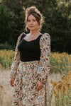 Woman in a floral dress standing in a field with trees in the background