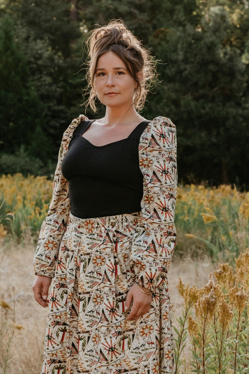 Woman in a floral dress standing in a field with trees in the background